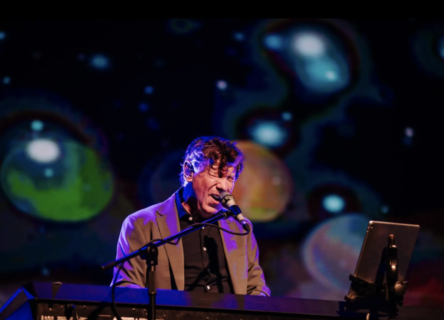 Flávio Venturini ao piano com projeção colorida ao fundo